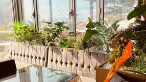 Una habitación moderna con una mesa de vidrio, asientos acolchados y ventanas amplias con vista a la ciudad.