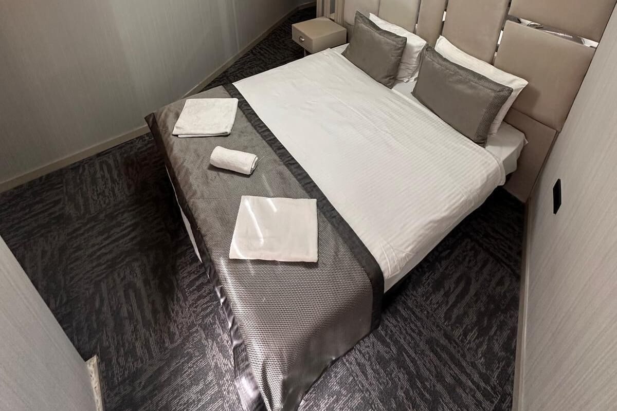 A modern hotel room with a large bed, a bedside table, a nightstand, and a unique ceiling light fixture.