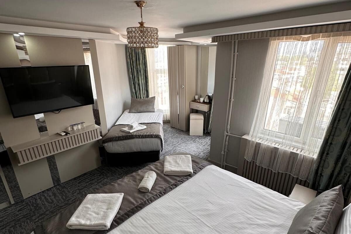 A hotel room with a large bed, a TV, a desk, and a window with curtains.