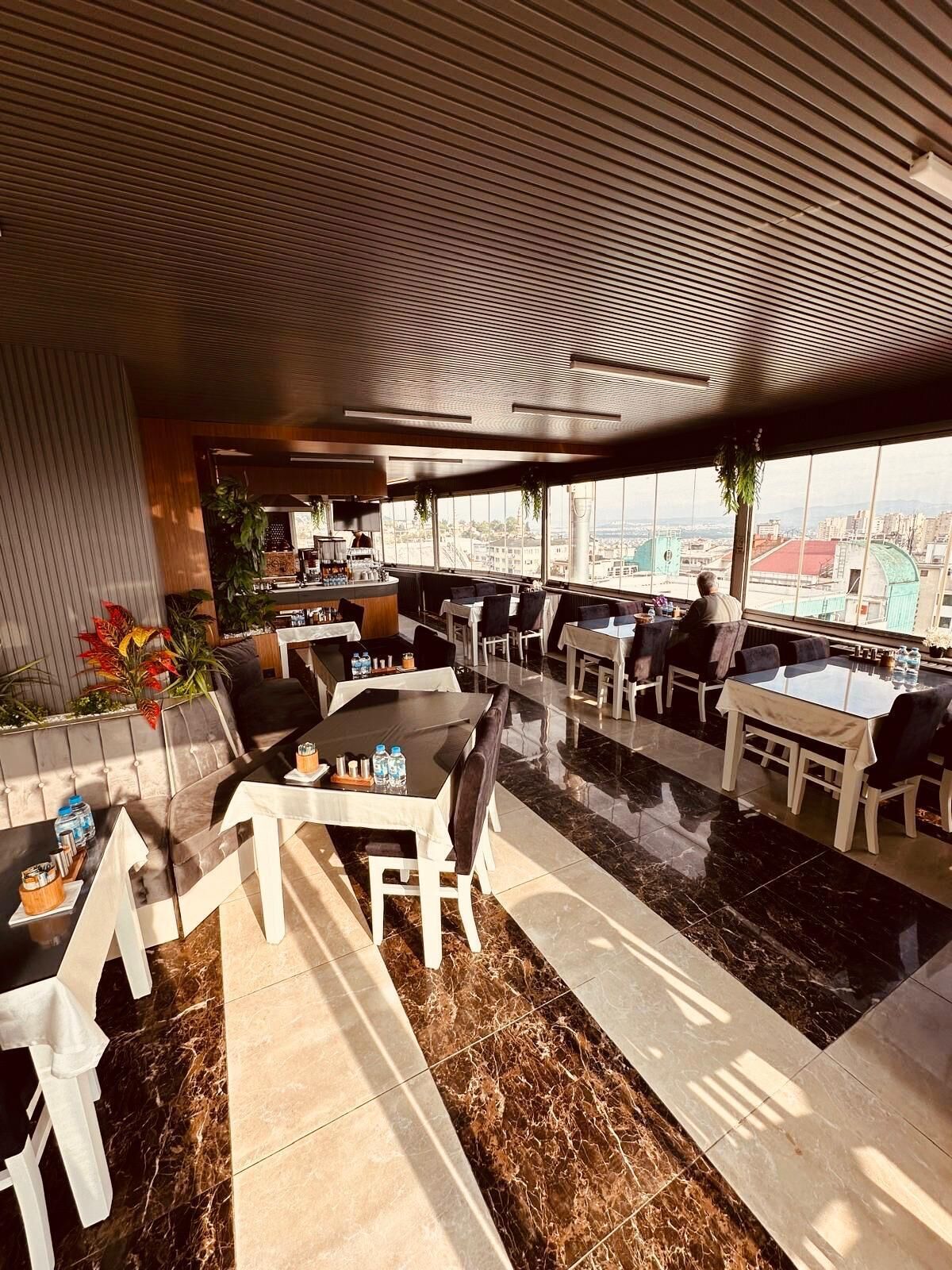 Eine Dachterrasse mit mehreren Sitzbereichen, darunter Tische und Stühle, und Blick auf die Stadtlandschaft.