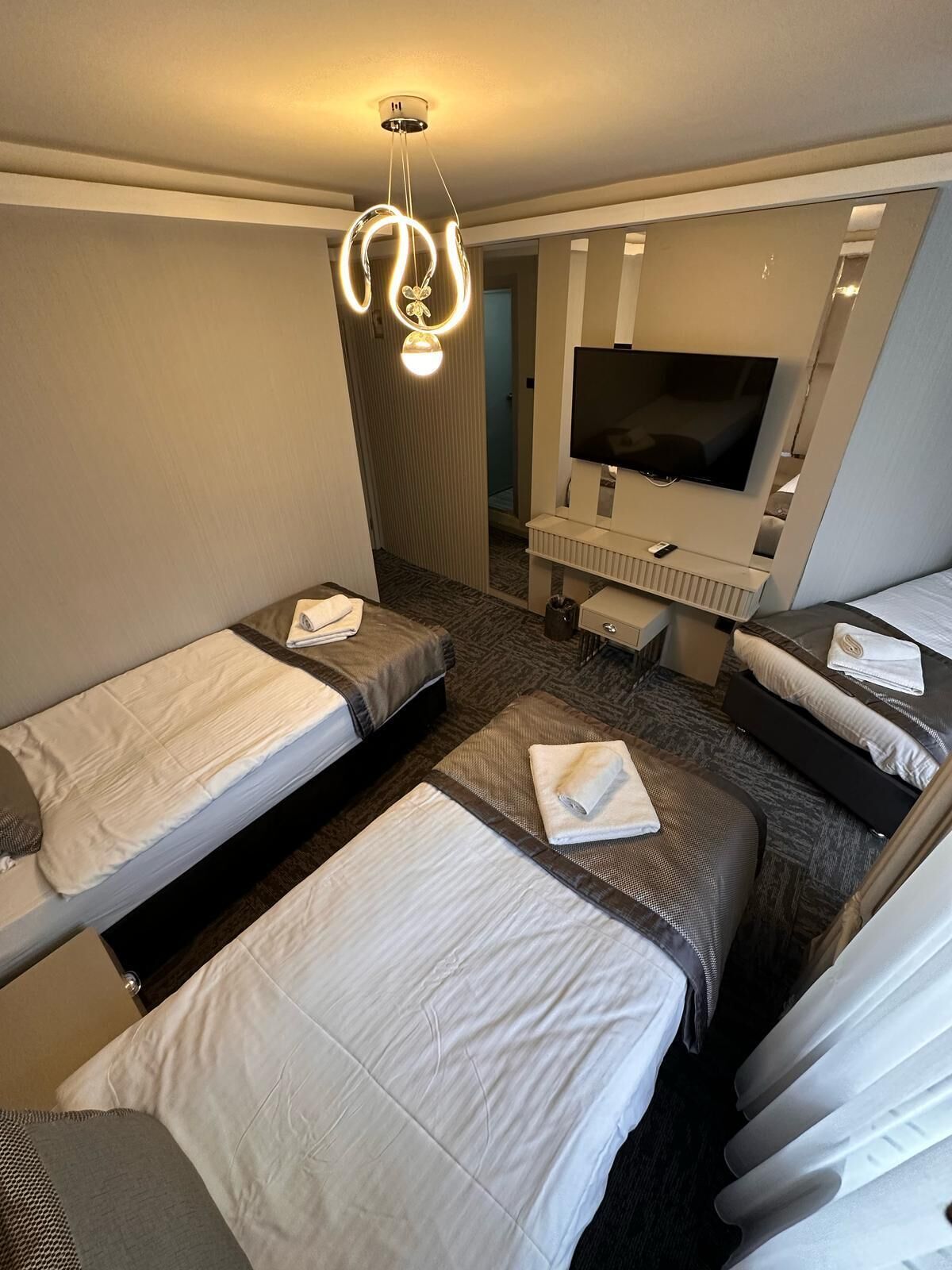 Habitación de hotel con dos camas individuales, televisión, un escritorio pequeño y un espejo.