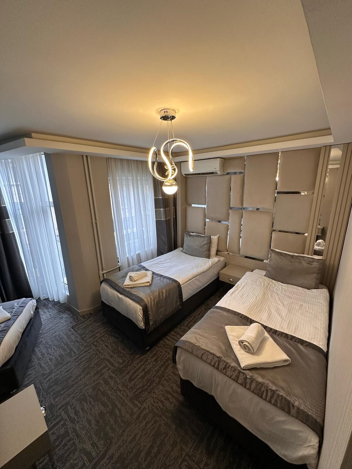 Une chambre d’hôtel avec deux lits, un grand miroir et un luminaire moderne.