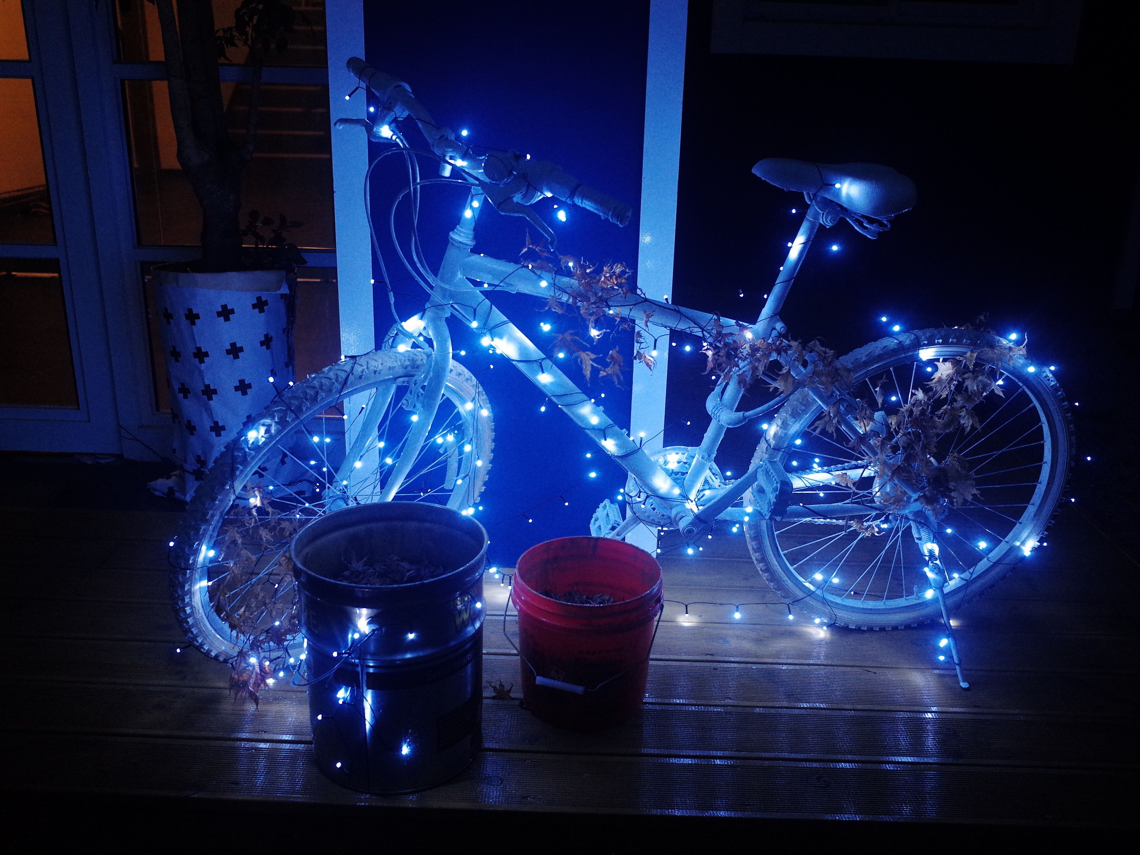 Una bicicleta adornada con luces azules, un cubo negro y un cubo rojo sobre una superficie de madera.