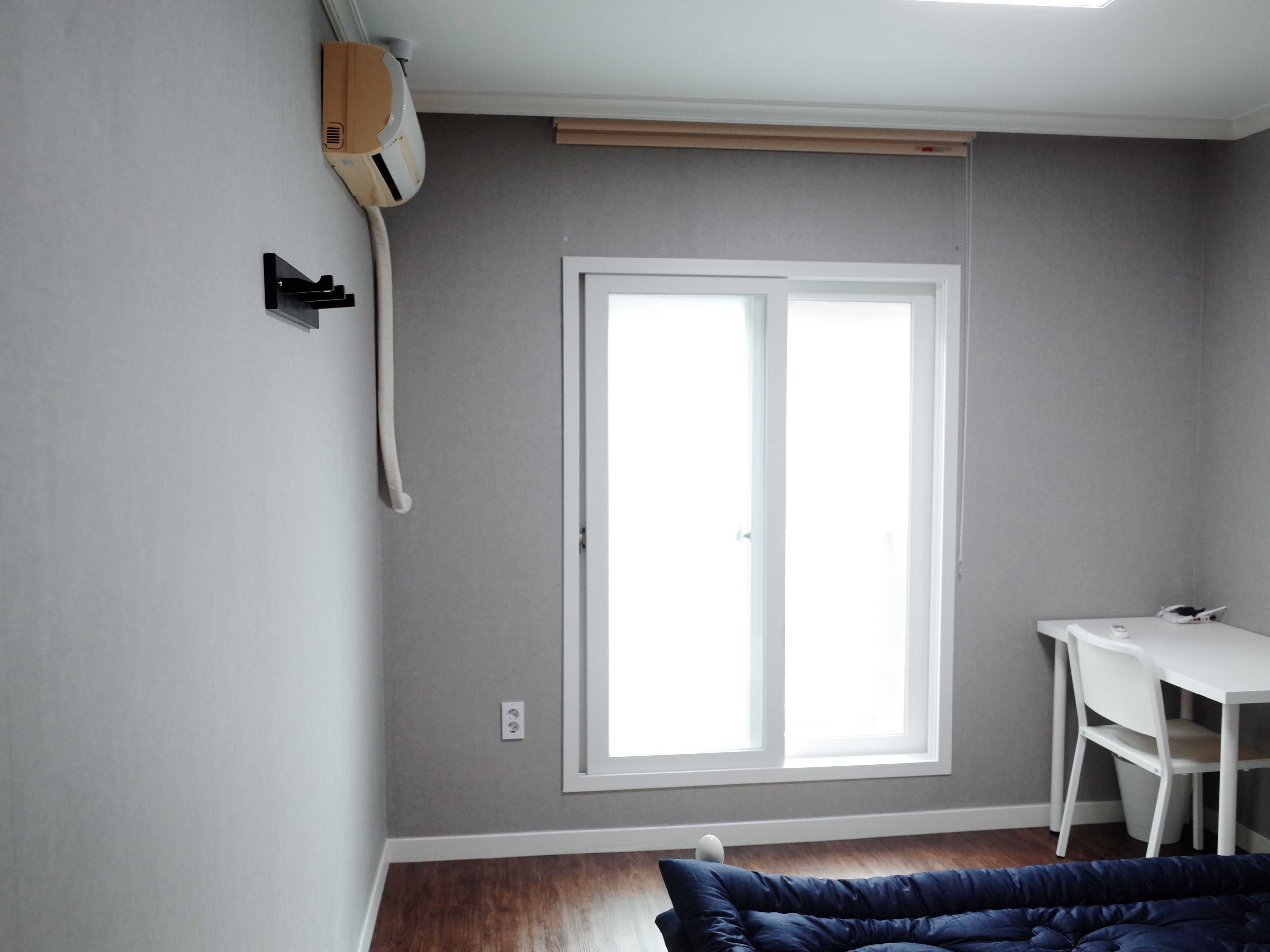 A room with a large window, a white desk, and a blue sofa.