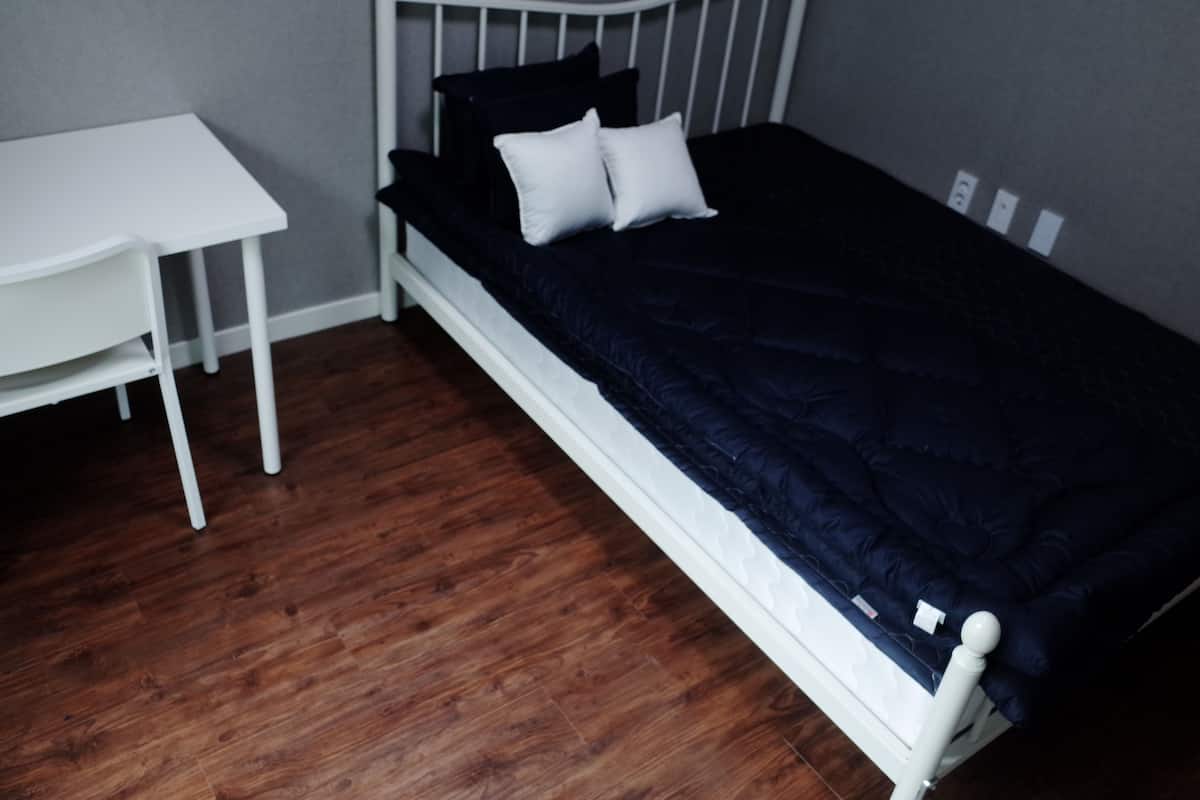 A small, neatly arranged bedroom with a single bed, a white nightstand, and a wooden floor.