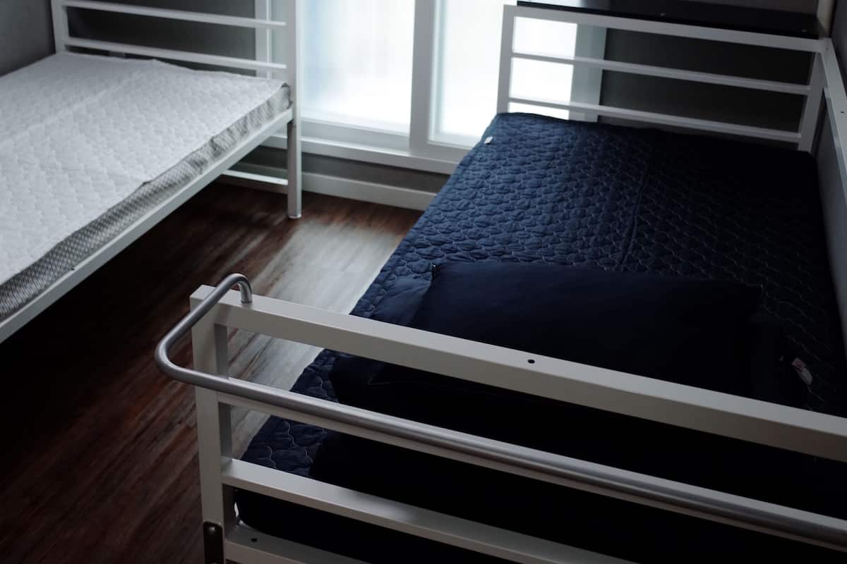 A bedroom with two bunk beds, a window with blinds, and a wooden floor.