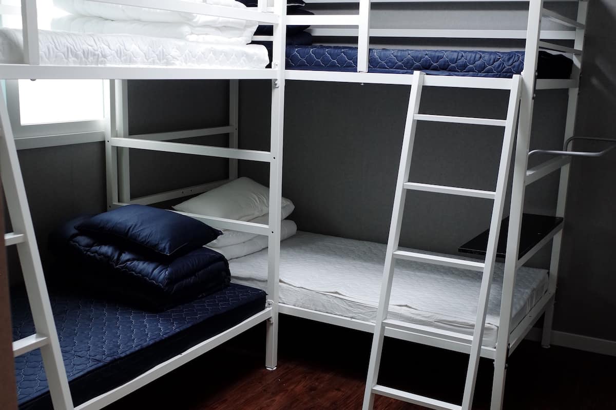 A bunk bed room with a wooden floor, grey walls, and a window.