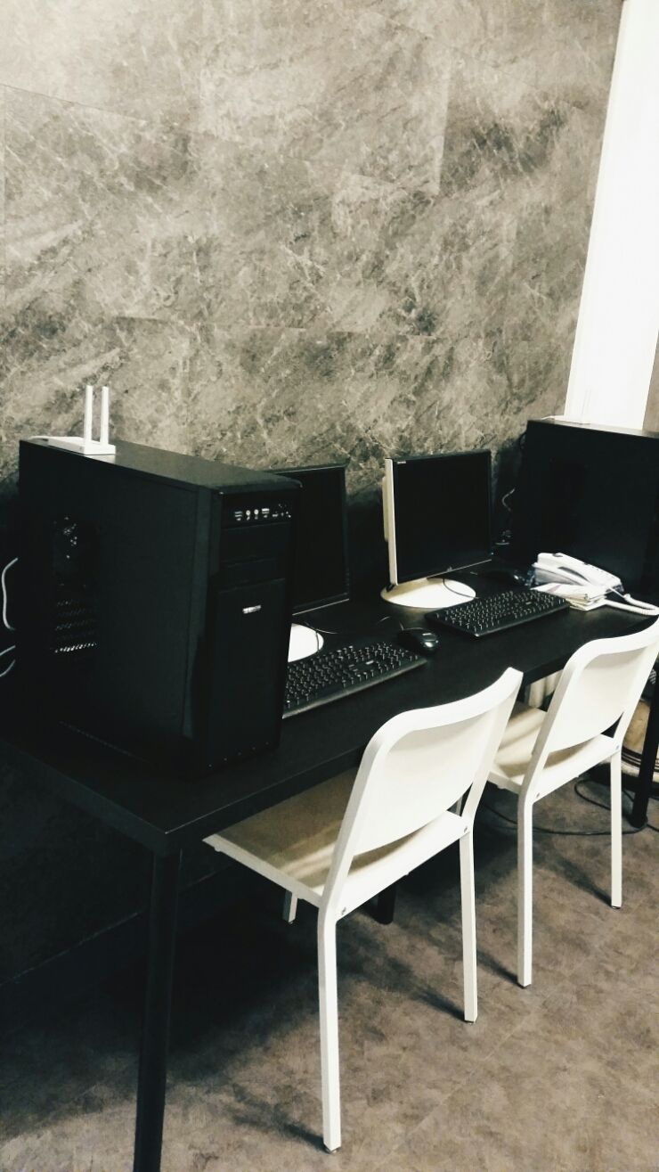 A room with a black desk, two computer monitors, a keyboard, and a mouse. There are two white chairs and a white telephone.
