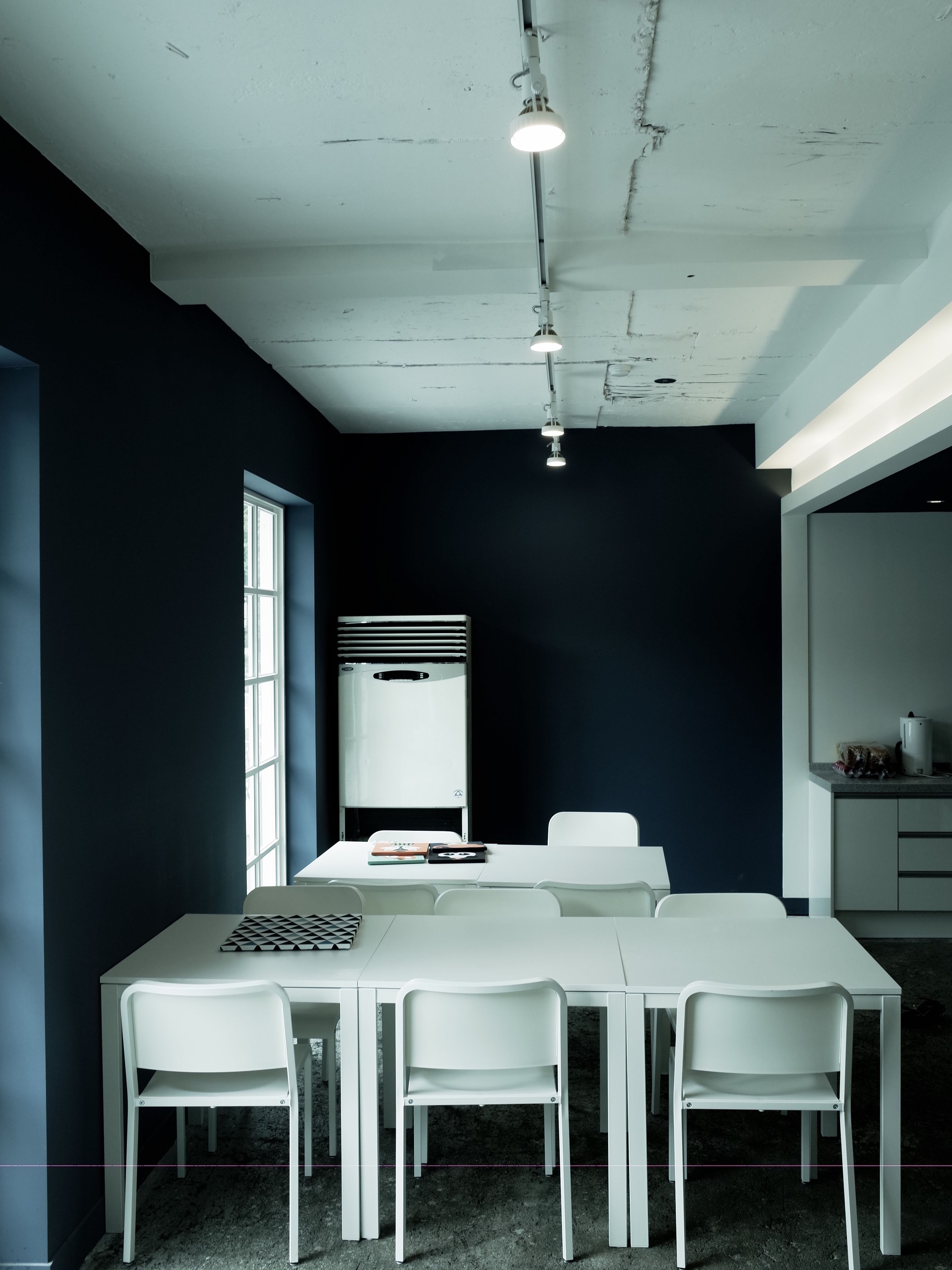 Une salle de conférence avec une table blanche, quatre chaises, un tableau blanc et une fenêtre.