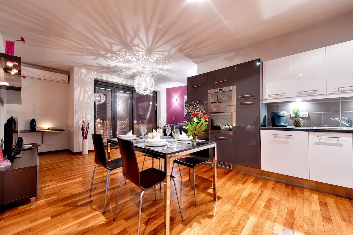 A modern kitchen with wooden flooring, a dining table set for four, and a decorative ceiling light.