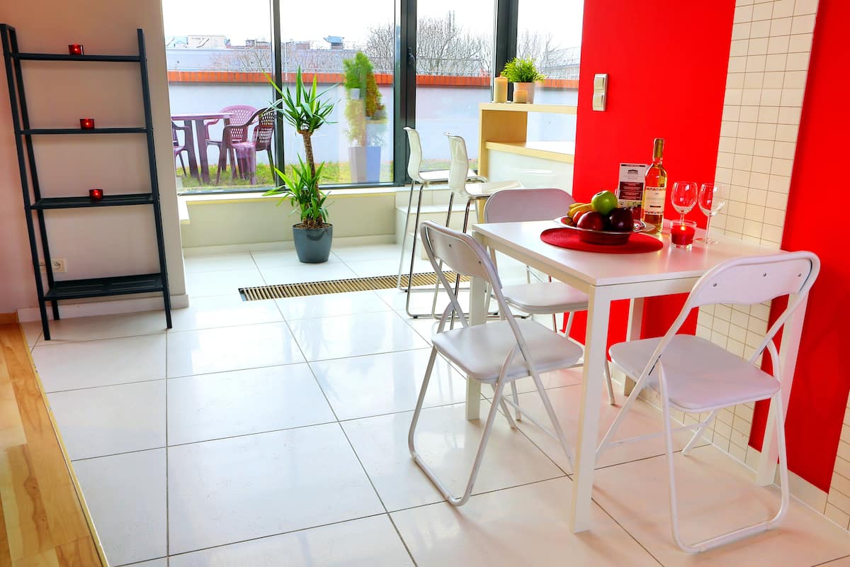 A dining area with a white table, four white chairs, a red table runner, and a potted plant.