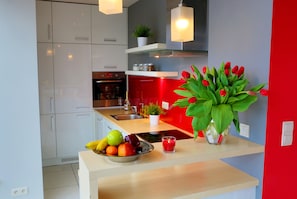 Uma cozinha moderna com armários brancos, uma cesta de frutas, uma vela e um vaso de tulipas vermelhas.