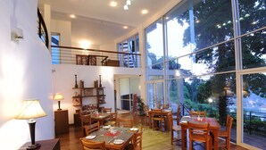 A spacious dining area with wooden tables and chairs, large windows offering a view of the outdoors, and a staircase leading to an upper level. - Hotel See Kandy (Kandy)