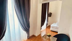 Una habitación moderna con suelo de madera, una mesa de vidrio, dos sillas azules y una cama con ropa blanca.