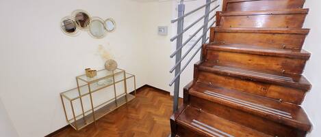 A wooden staircase with a metal handrail, a glass console table with decorative items, and a herringbone-patterned wooden floor.