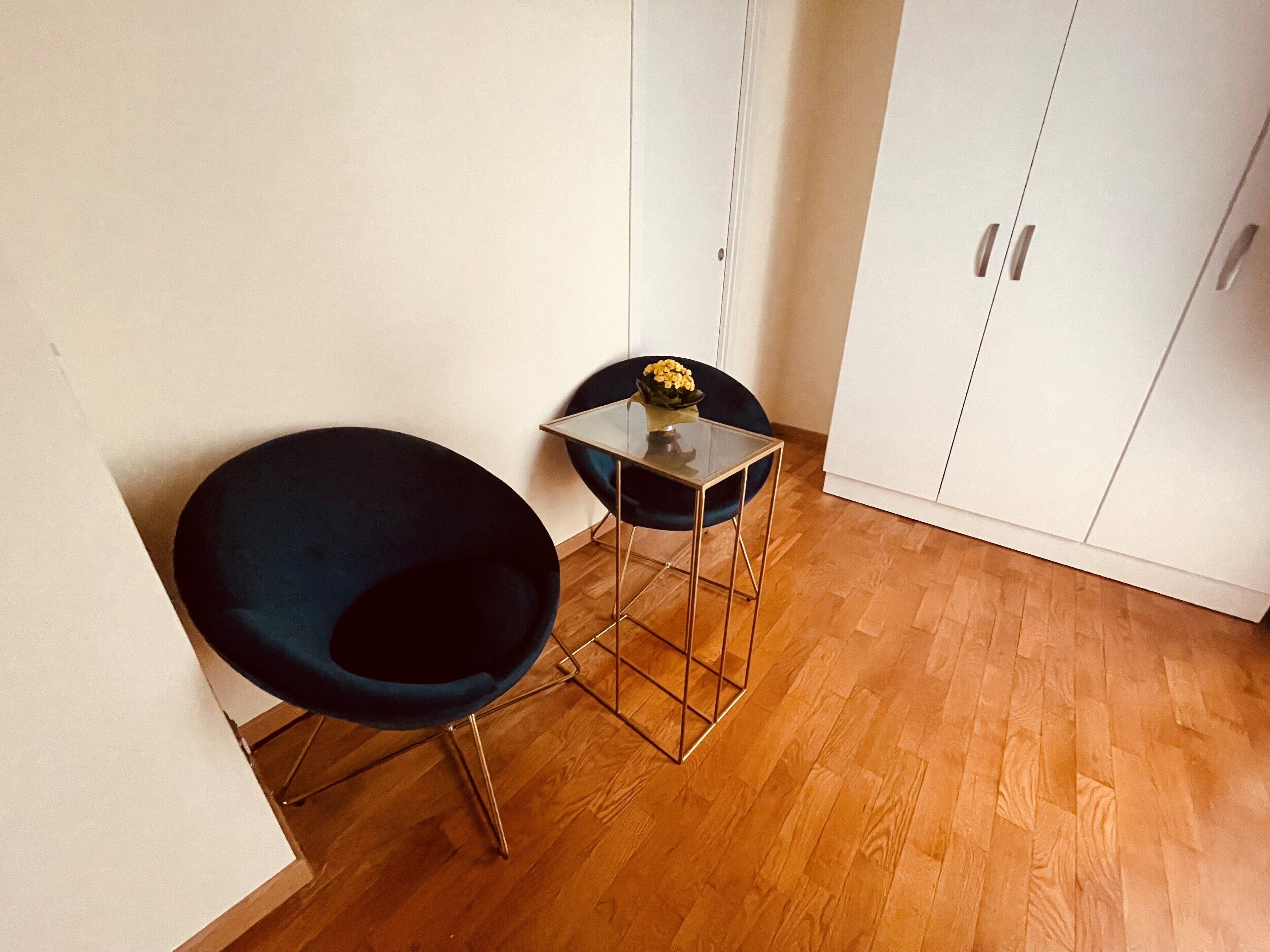 A corner room with a dark blue chair, a small glass table, and a white wardrobe.