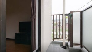 A narrow corridor with a staircase leading to a balcony. A dark-colored piece of furniture is placed against the wall. - Sunlife Yamashina Apartment (Kyoto)