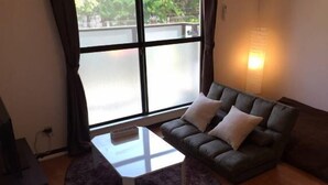A modern living room with a dark grey sofa, two white cushions, a small white table, and a purple rug. - Sunlife Yamashina Apartment (Kyoto)