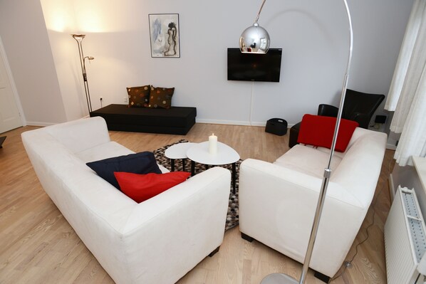 A modern living room with two white sofas, a floor lamp, a black TV stand, and a painting on the wall.
