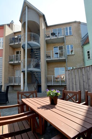 A multi-story apartment building with balconies, a wooden table with chairs, and a potted plant.