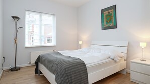 Un dormitorio ordenado con cama, mesitas de noche, una lámpara de pie y una ventana con persianas.