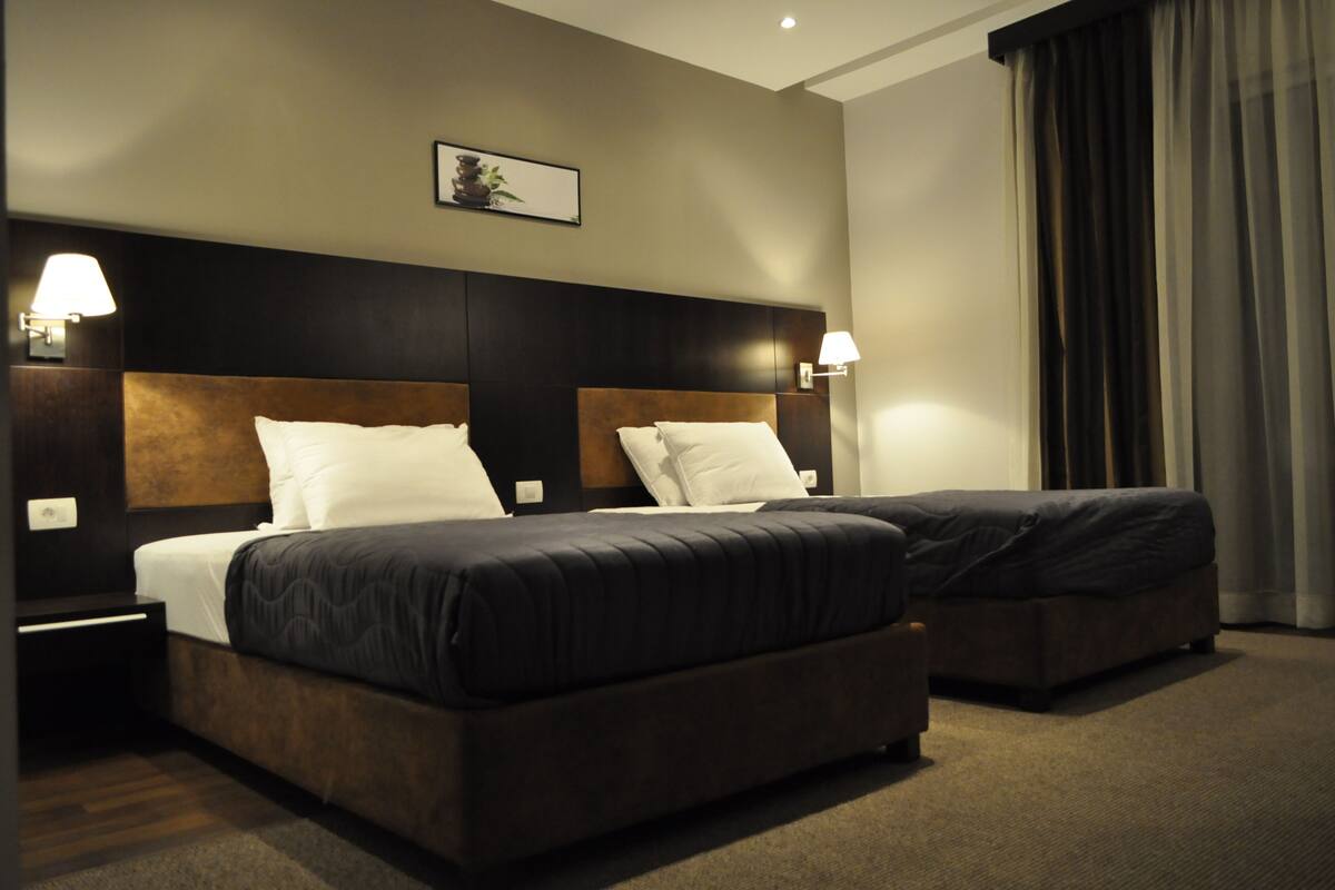 Una habitación de hotel con dos camas, cabeceros oscuros y lámparas de noche.