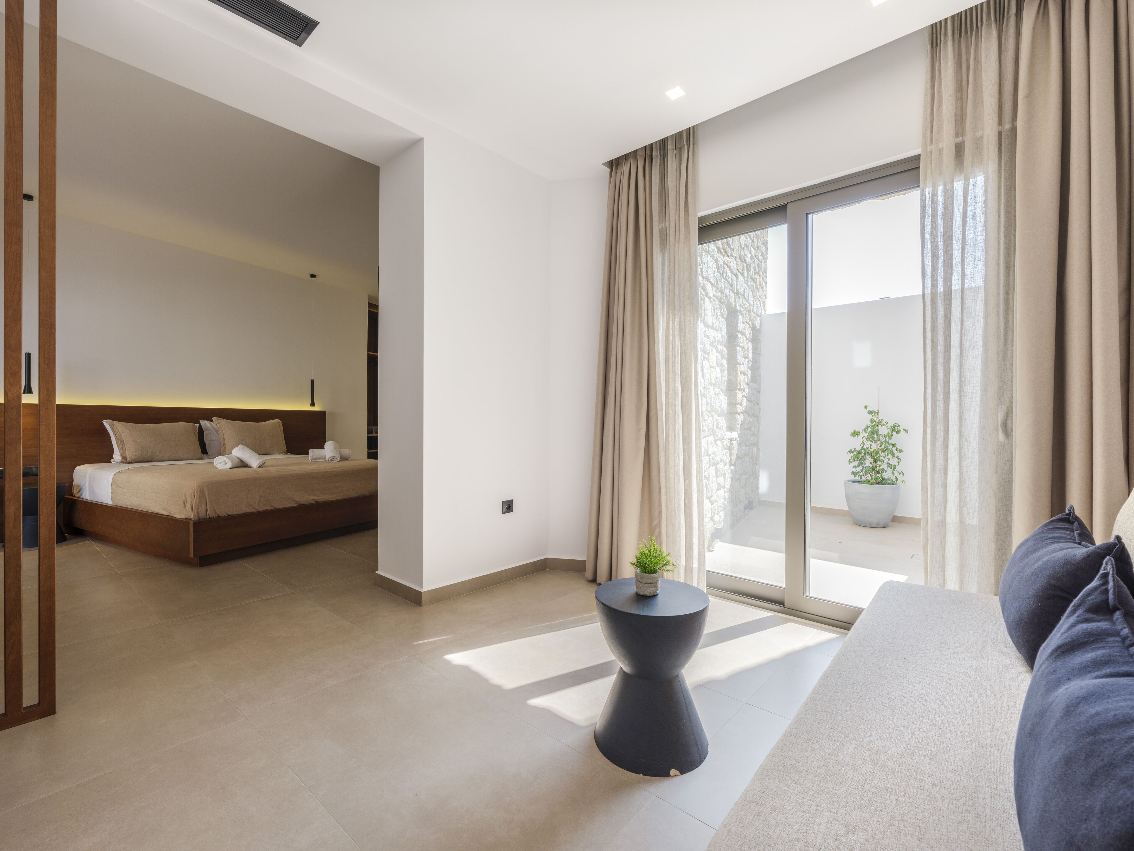 Een moderne hotelkamer met een bed, een klein nachtkastje en een groot raam met gordijnen.