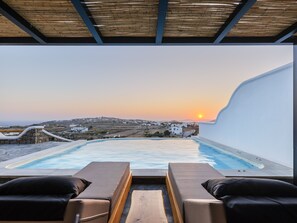 A poolside lounge with a view of a sunset over a coastal village. - Evi Suites & Villas (Mykonos)