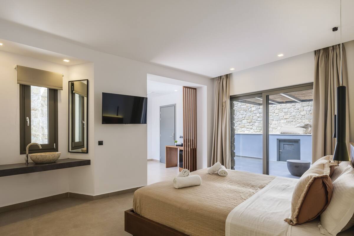 A modern bedroom with a large bed, a built-in TV, a stone wall, and a balcony with a stone floor.