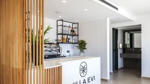 A modern reception area with a wooden slat partition, a coffee machine, and a shelf with various items. - Evi Suites & Villas (Mykonos)