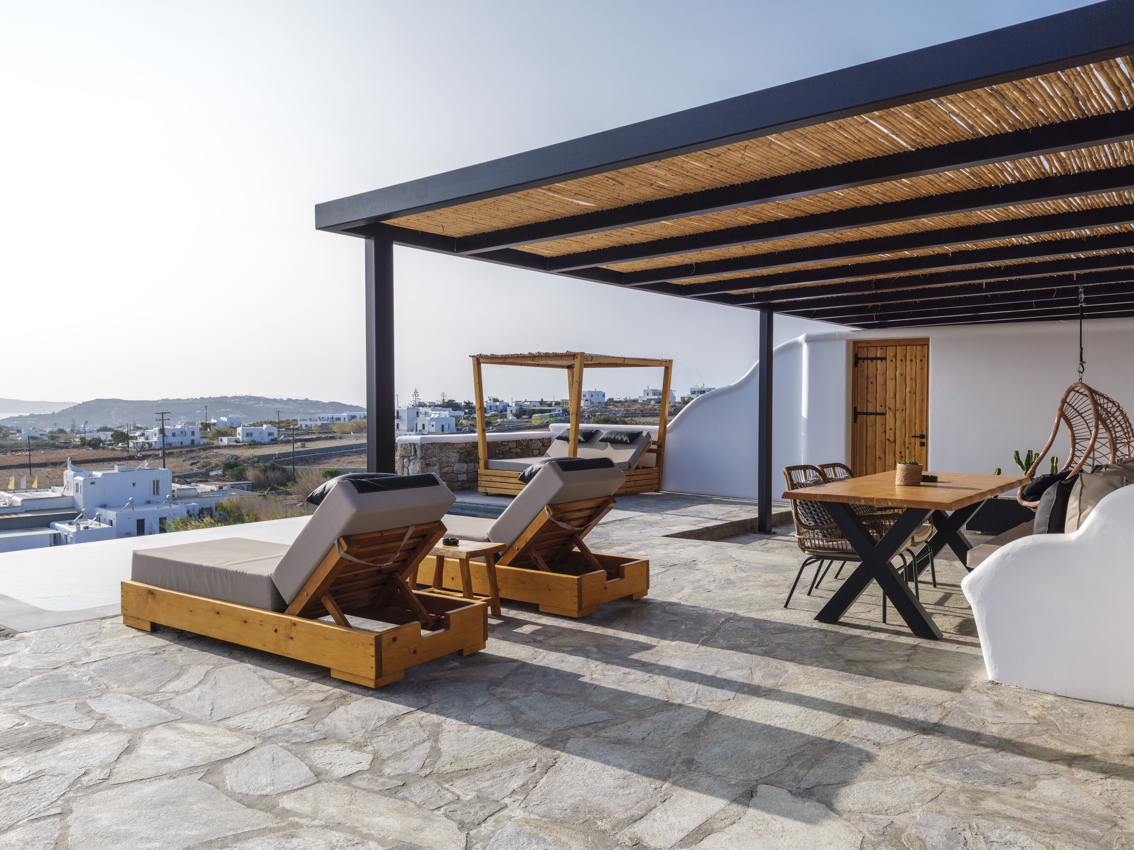 A rooftop terrace with stone flooring, wooden lounge chairs, a wooden table, and a hanging chair.