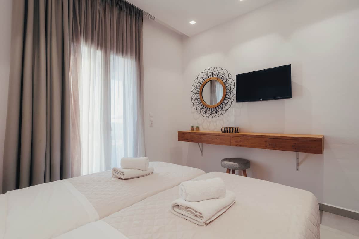 A hotel room with two beds, a TV, a wooden shelf, and a large window with curtains.