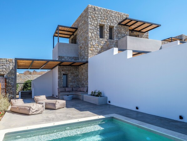 A modern house with a stone exterior, a swimming pool, and outdoor seating. - Evi Suites & Villas (Mykonos)