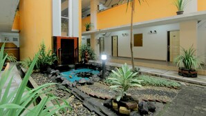 A hotel courtyard with a small pond, potted plants, and a palm tree. - University Hotel Yogyakarta (Yogyakarta)