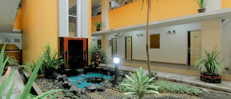 A hotel courtyard with a small pond, potted plants, and a palm tree.
