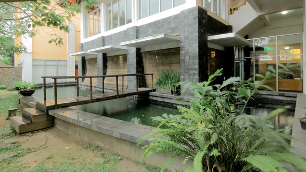 A modern building with a pool, a bridge, and surrounding greenery. - University Hotel Yogyakarta (Yogyakarta)