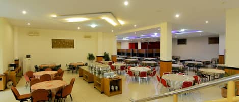 A spacious dining area with multiple tables and chairs, a staircase, and a ceiling with recessed lighting.
