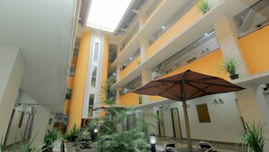 A multi-level atrium with yellow and white walls, potted plants, and a large umbrella. - University Hotel Yogyakarta (Yogyakarta)