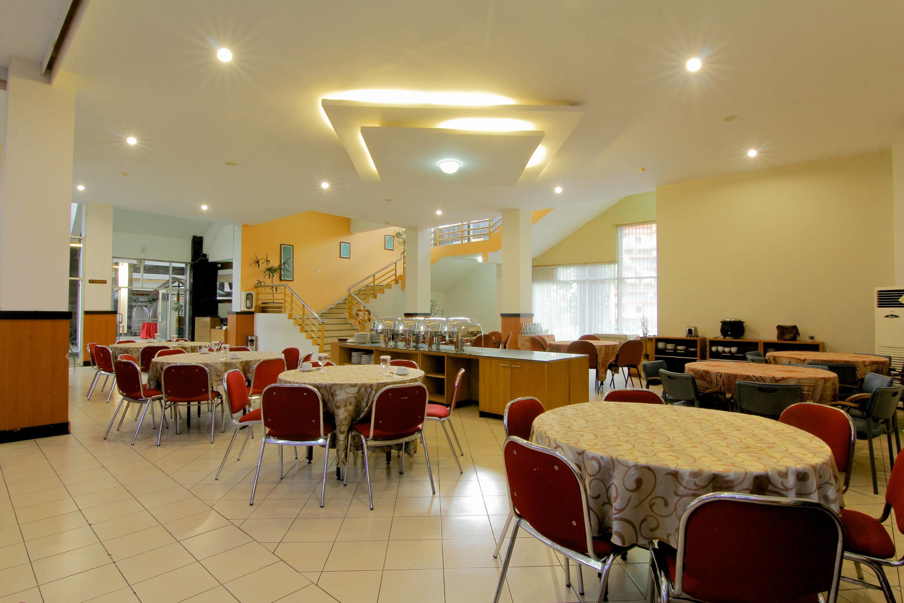 Comedor con varias mesas y sillas, una escalera y una zona de cocina.