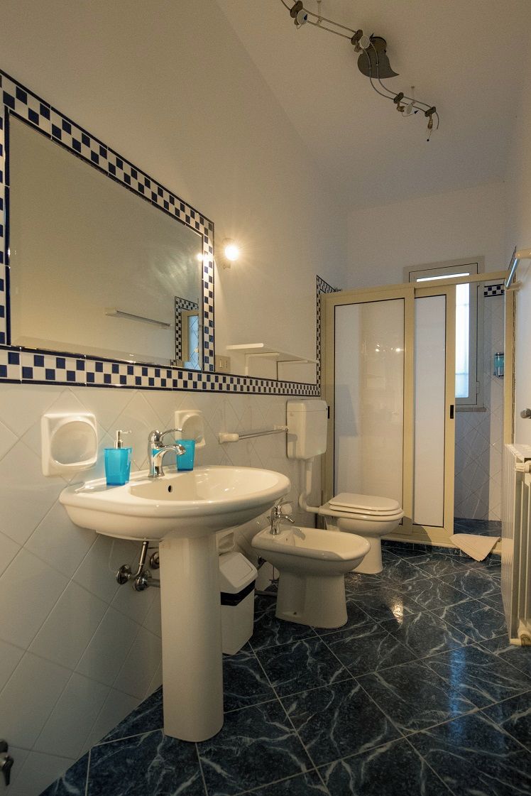 A bathroom with a sink, toilet, bidet, and a mirror with a checkered border.