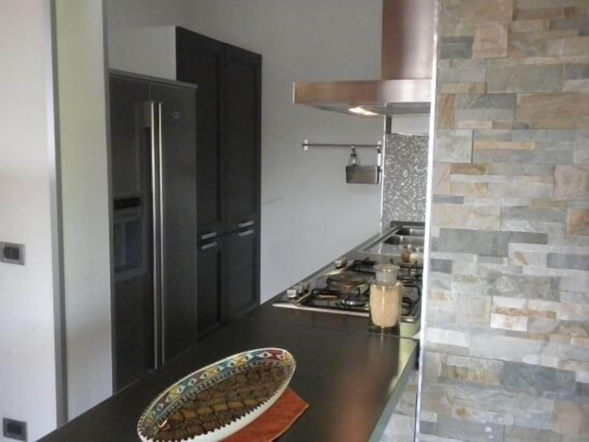 A modern kitchen with a stainless steel refrigerator, a gas stove, and a stone backsplash.