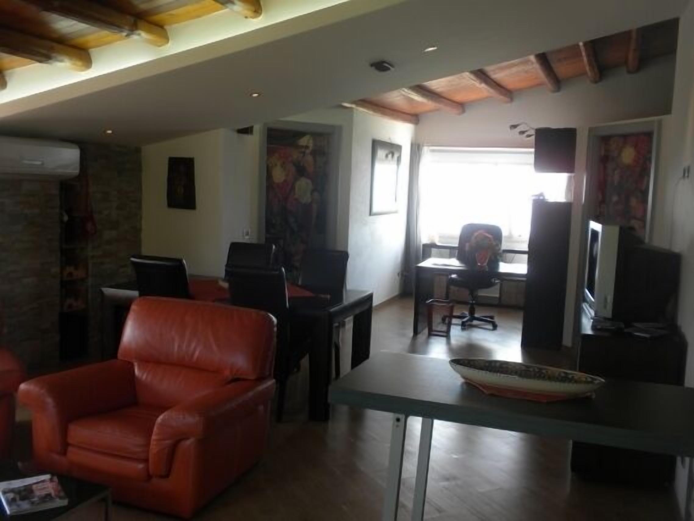 Una sala de estar con un sofá de cuero rojo, una mesa de comedor con un bol y un televisor sobre un mueble.