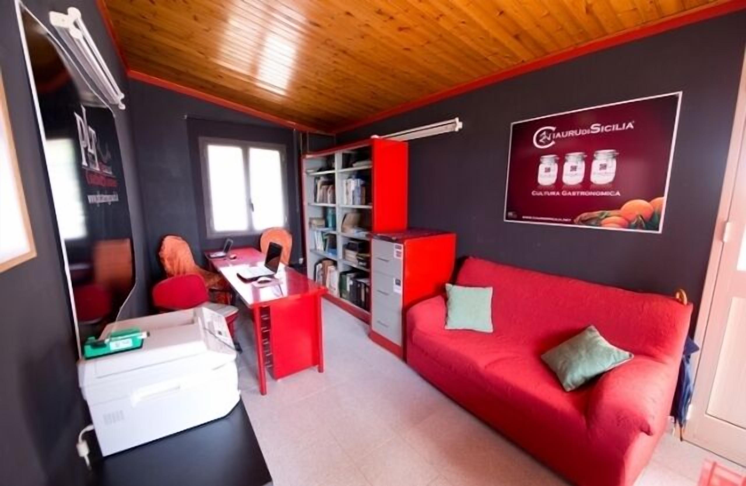 Ein kompakter Wohnbereich mit einem roten Sofa, einem kleinen Schreibtisch und einem Bücherregal.