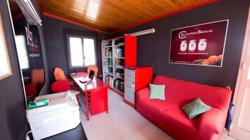 Ein kompakter Wohnbereich mit einem roten Sofa, einem kleinen Schreibtisch und einem Bücherregal.