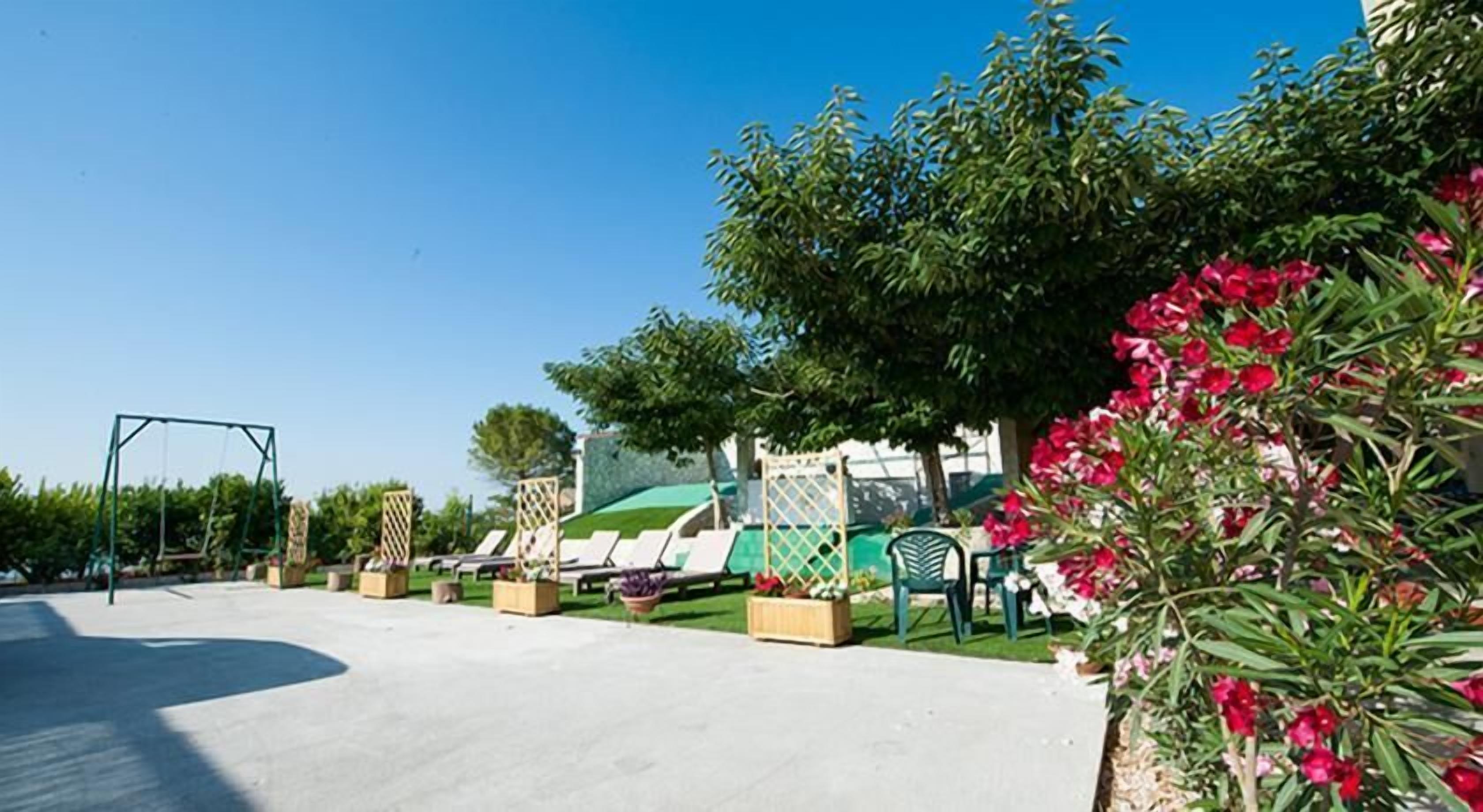 A playground area with swings, a slide, and a green climbing structure. There are lounge chairs and a table with a green tablecloth.