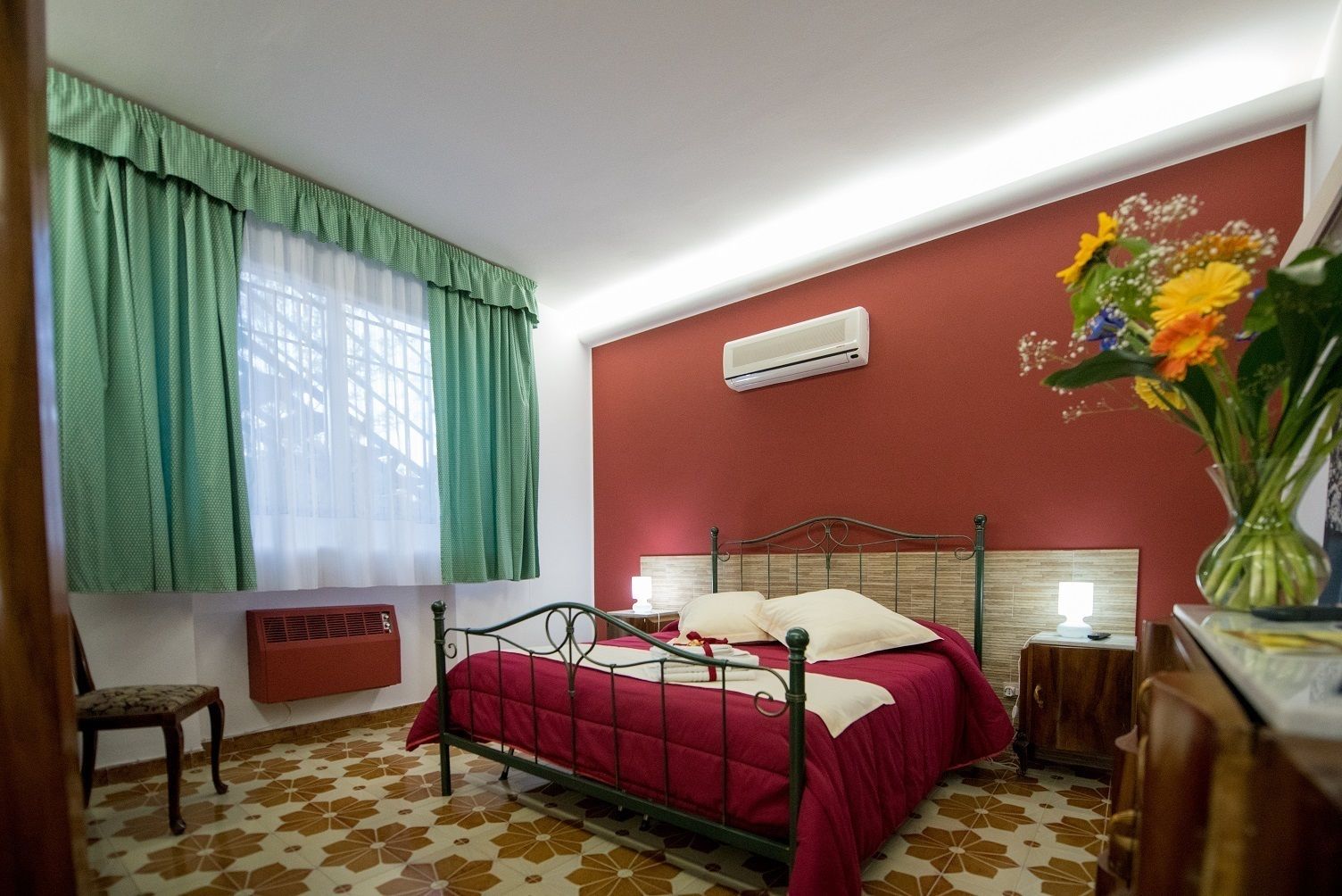 Une chambre à coucher comprenant un lit, une chaise, une table de chevet, un climatiseur fixé au mur et une fenêtre avec des rideaux.