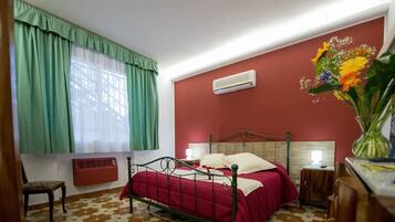 Une chambre à coucher comprenant un lit, une chaise, une table de chevet, un climatiseur fixé au mur et une fenêtre avec des rideaux.