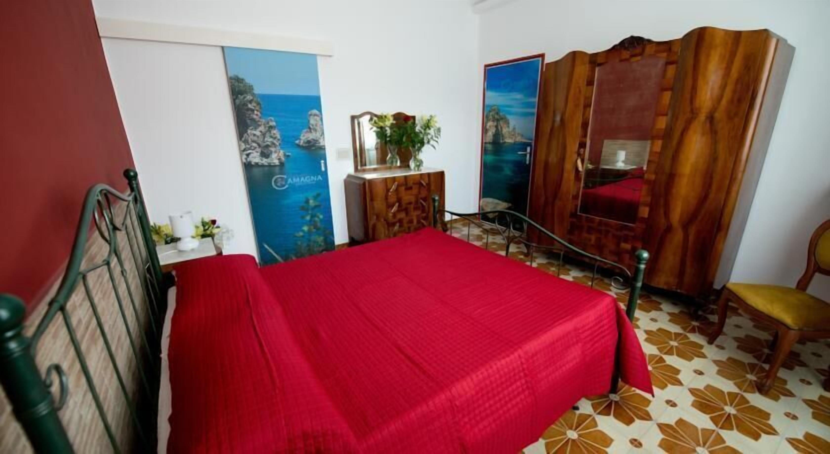 Un dormitorio con cama, un armario de madera, una mesita con un jarrón y una silla.