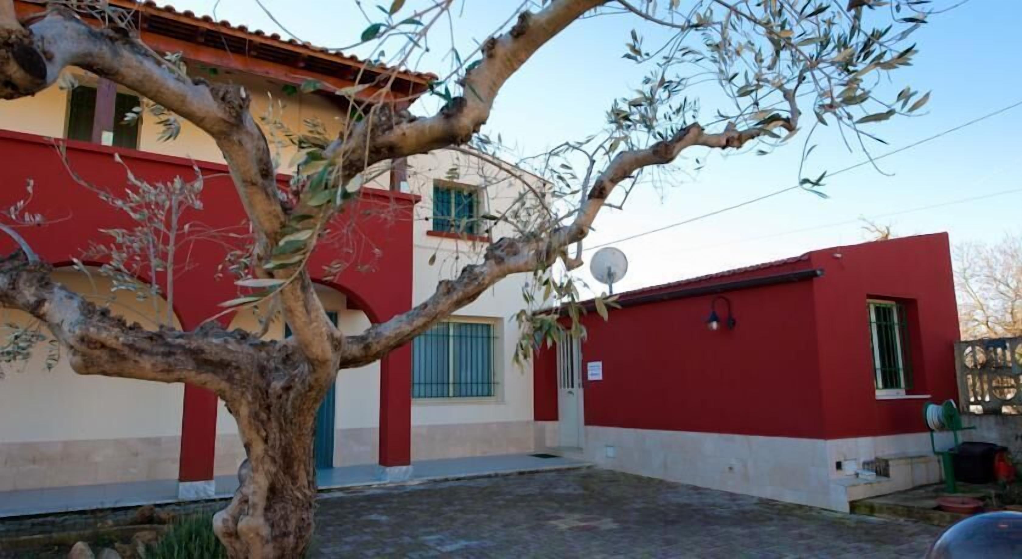 A two-story building with a red and beige facade, a satellite dish, and a tree in the foreground.
