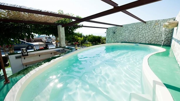 A swimming pool with a stone wall and a pergola structure. - Camagna Country House (Partanna)